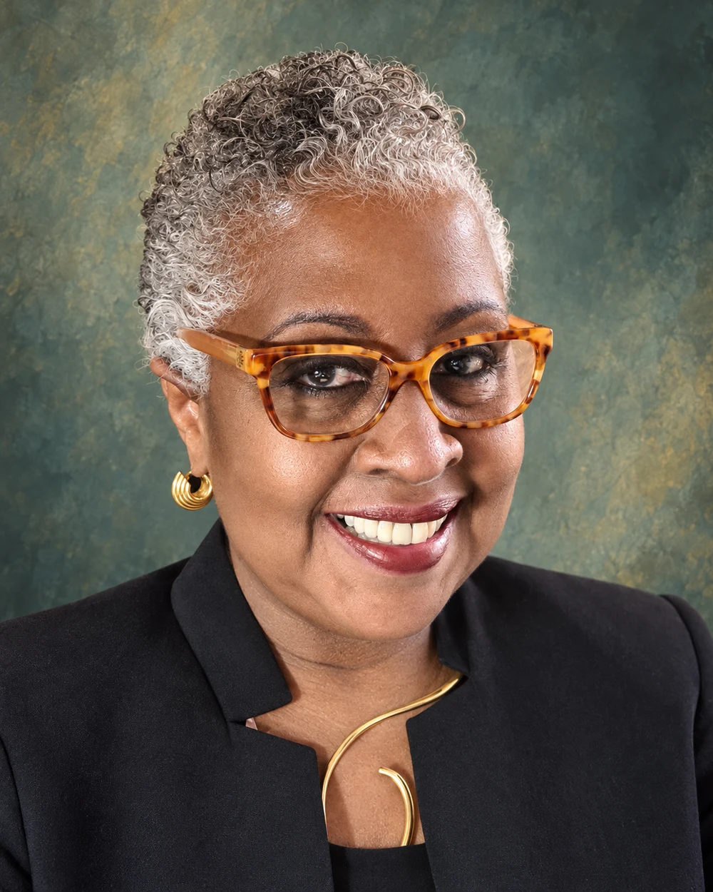 Sharon Saunders smiling, wearing tortoiseshell glasses and a black jacket.